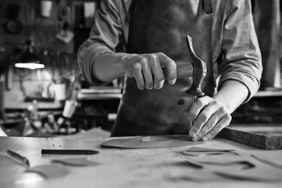 Le mani di un artigiano con il martello sul banco di lavoro, in bianco e nero